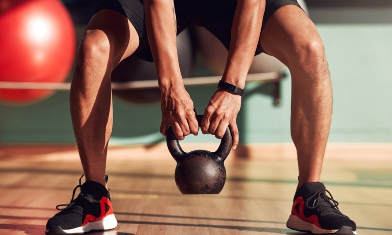 Muškarac drži kettlebell u teretani, fokusiran na vežbanje i jačanje mišića